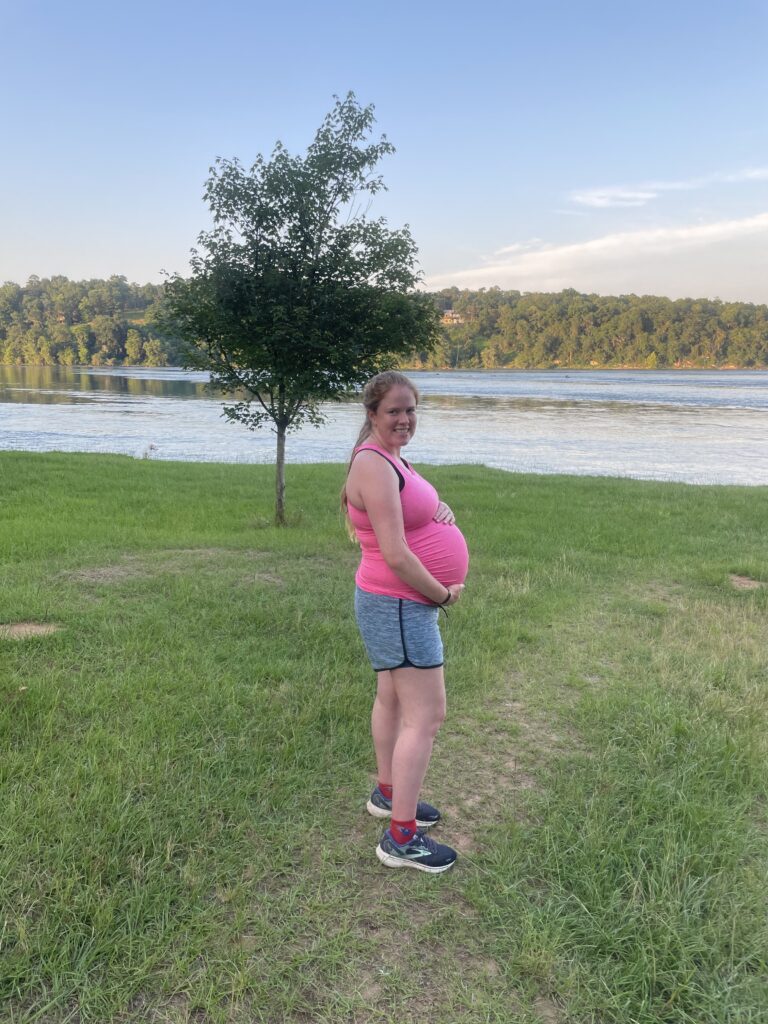 pregnant woman holding her belly while standing outside by water